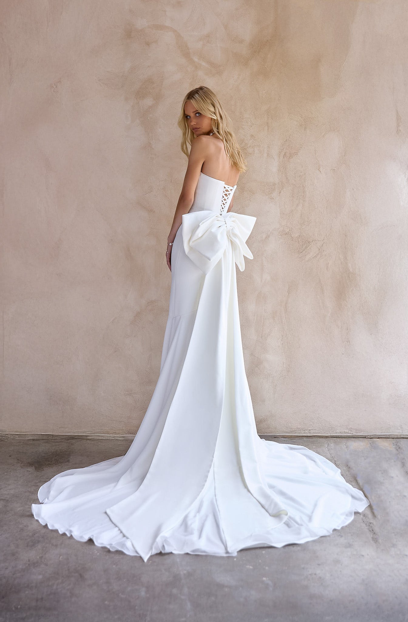 Back Image of the strapless June Wedding dress by The Bryde, featuring a detachable bow and pearl jewellery. Made from crepe main fabric and a soft chiffon angled skirt